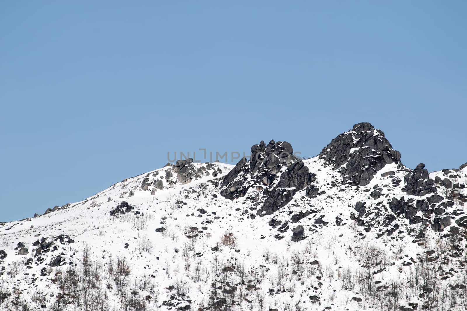 View of a rocky mountain peak covered with snow on a sunny day. Copy space.