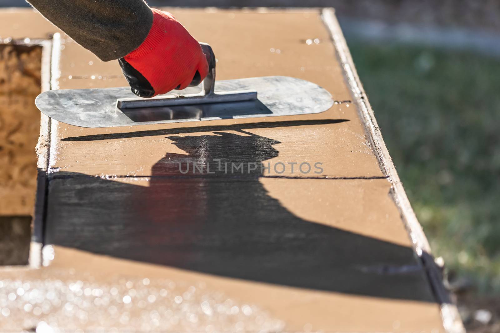 Construction Worker Using Trowel On Wet Cement Forming Coping Around New Pool.