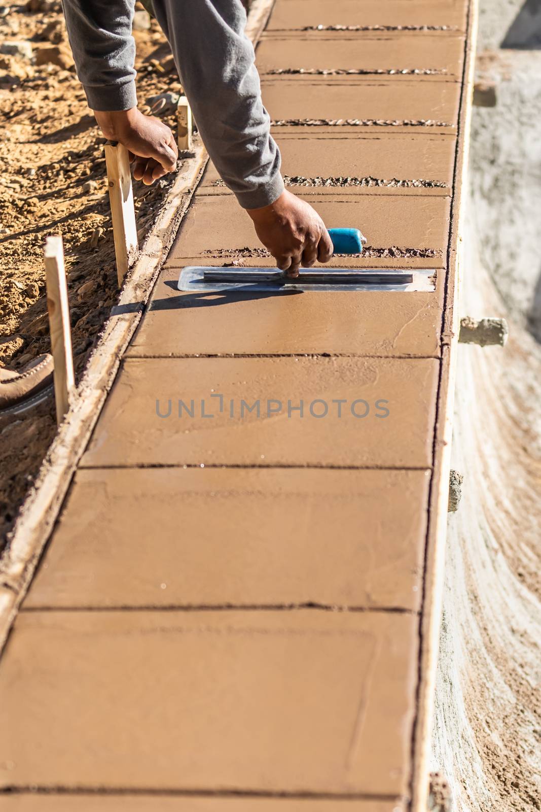 Construction Worker Using Trowel On Wet Cement Forming Coping Around New Pool.