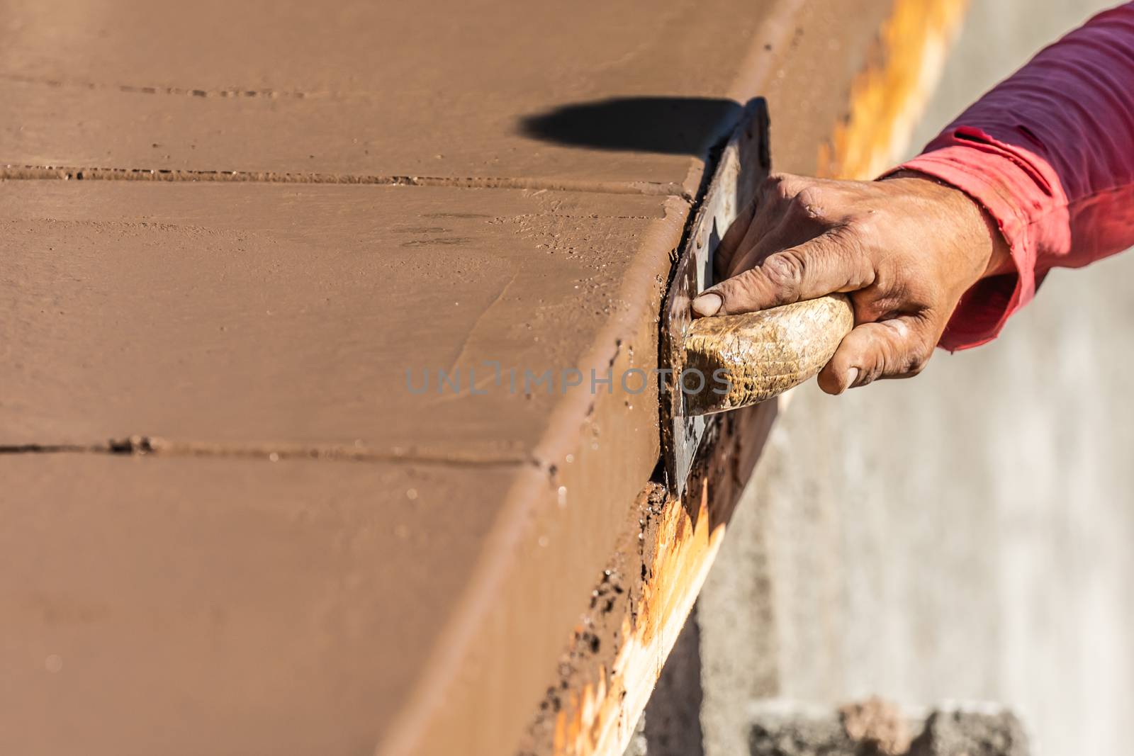 Construction Worker Using Wood Trowel On Wet Cement Forming Coping Around New Pool.