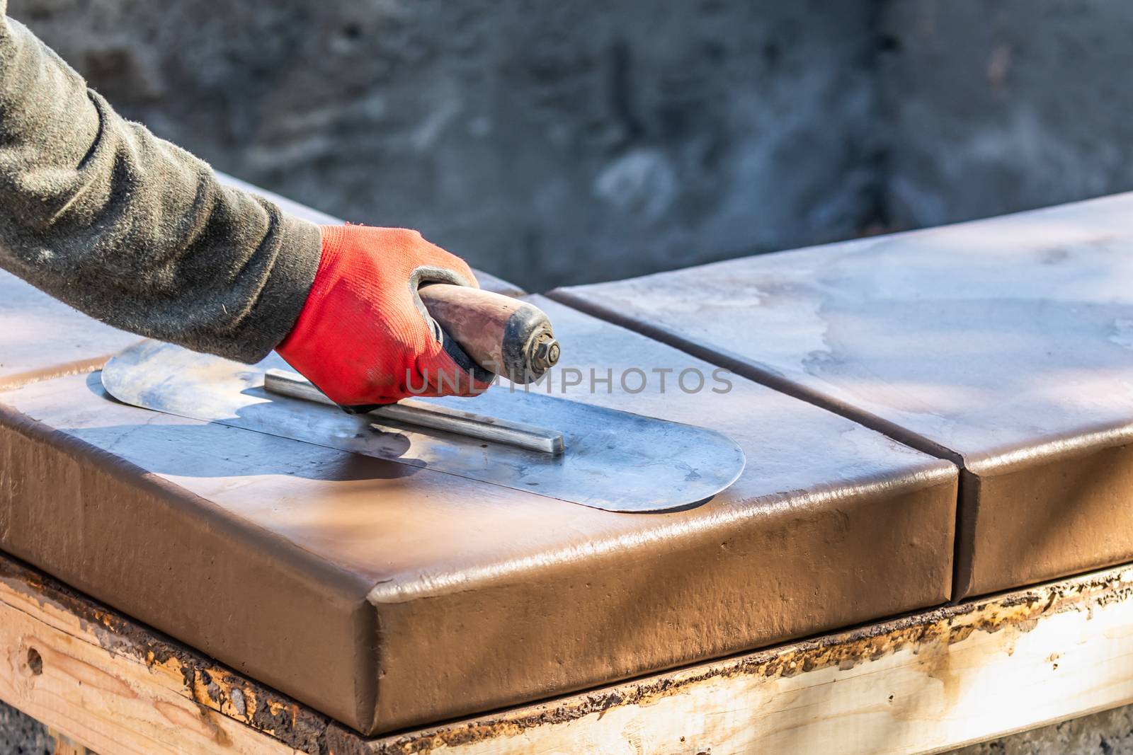 Construction Worker Using Trowel On Wet Cement Forming Coping Around New Pool.