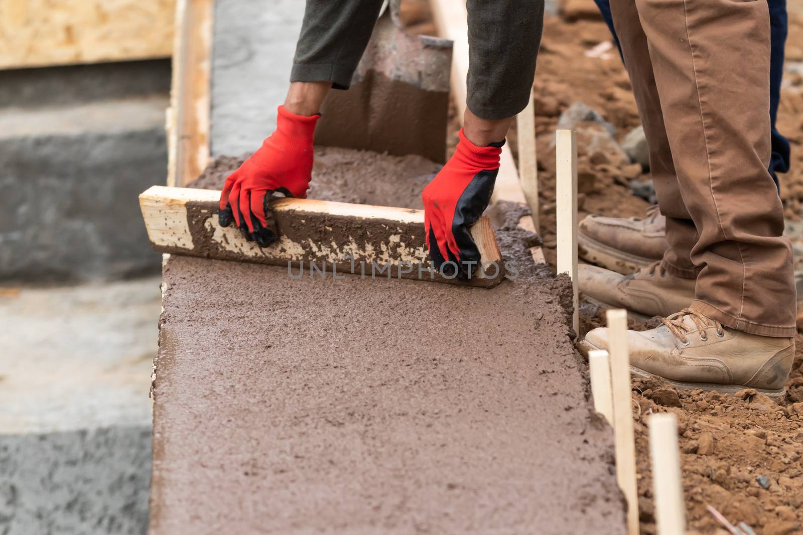 Construction Worker Leveling Wet Cement Into Wood Framing by Feverpitched