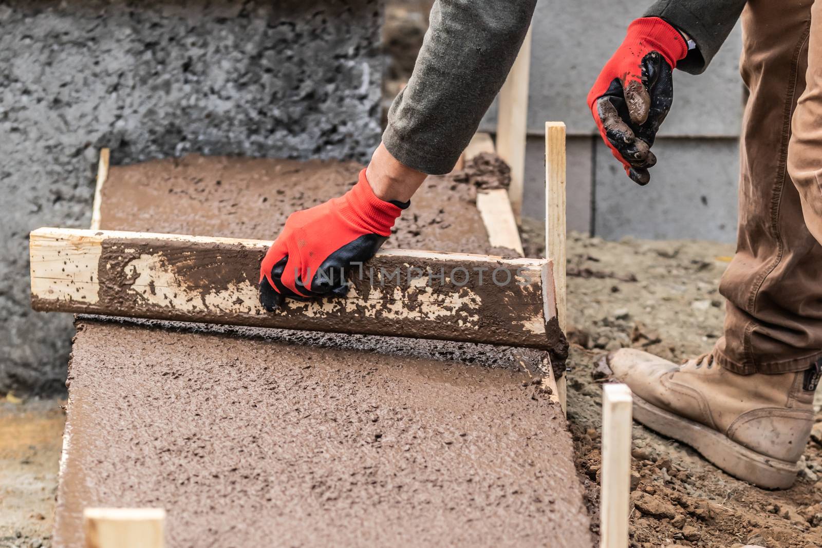 Construction Worker Leveling Wet Cement Into Wood Framing.