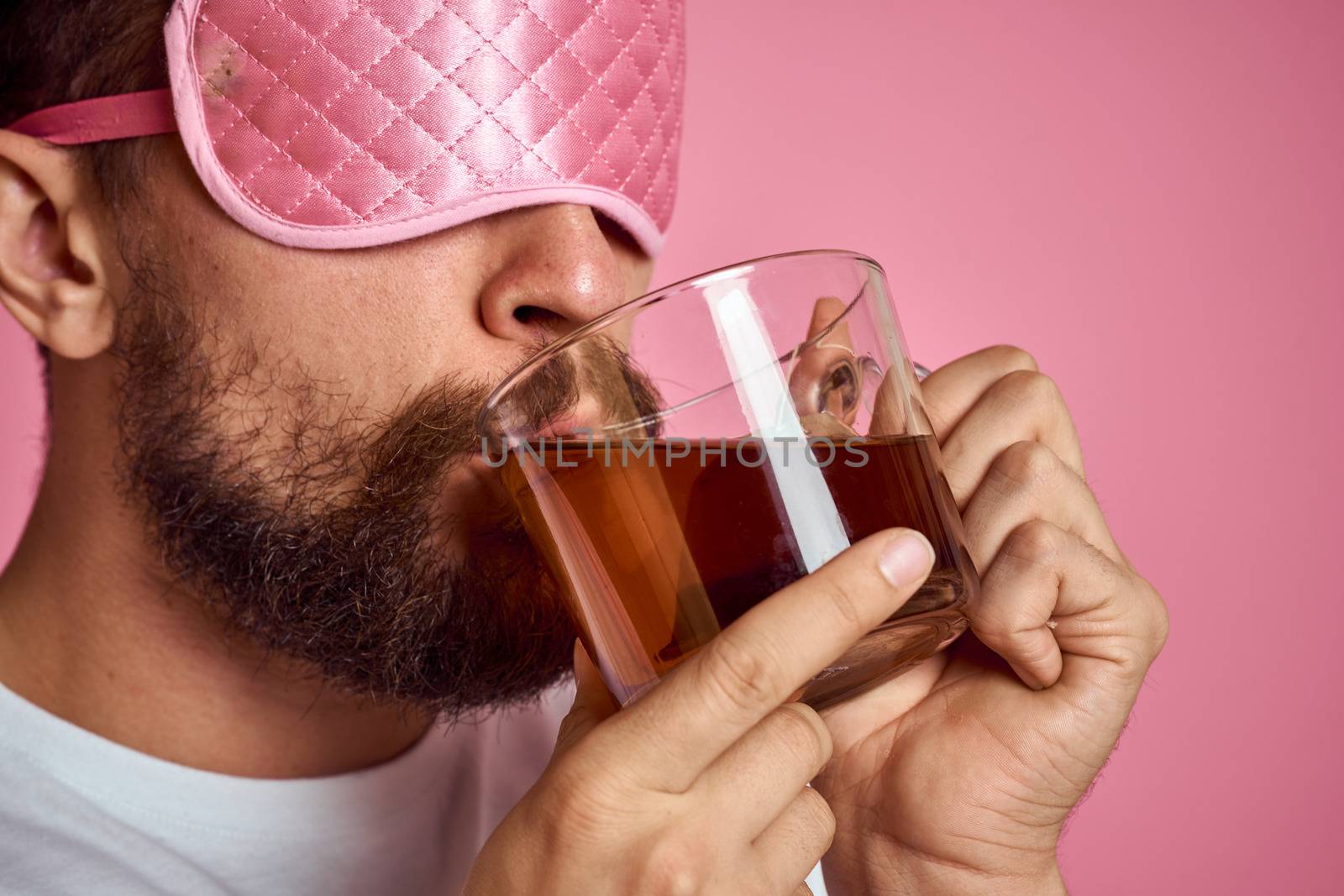 A man in a pink sleep mask with a cup of tea in his hands on an isolated background cropped view. High quality photo