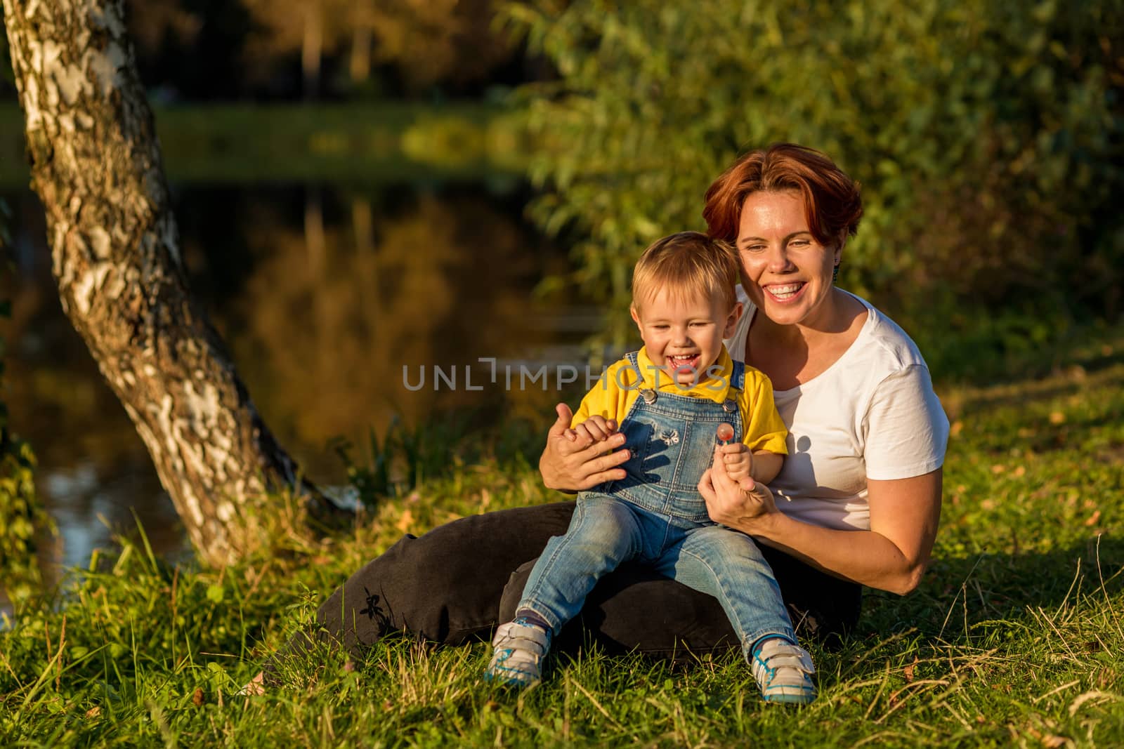 Mom and little boy sit on the river bank in the rays of the setting sun on an autumn evening