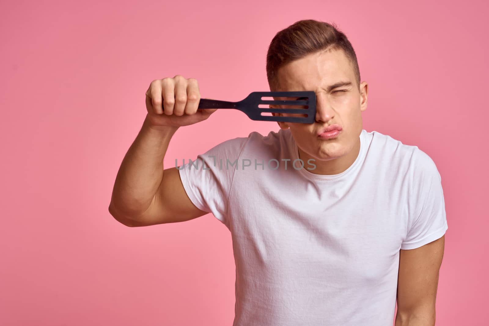 Man with kitchen tools on pink background spatula for cooking model cropped view. High quality photo