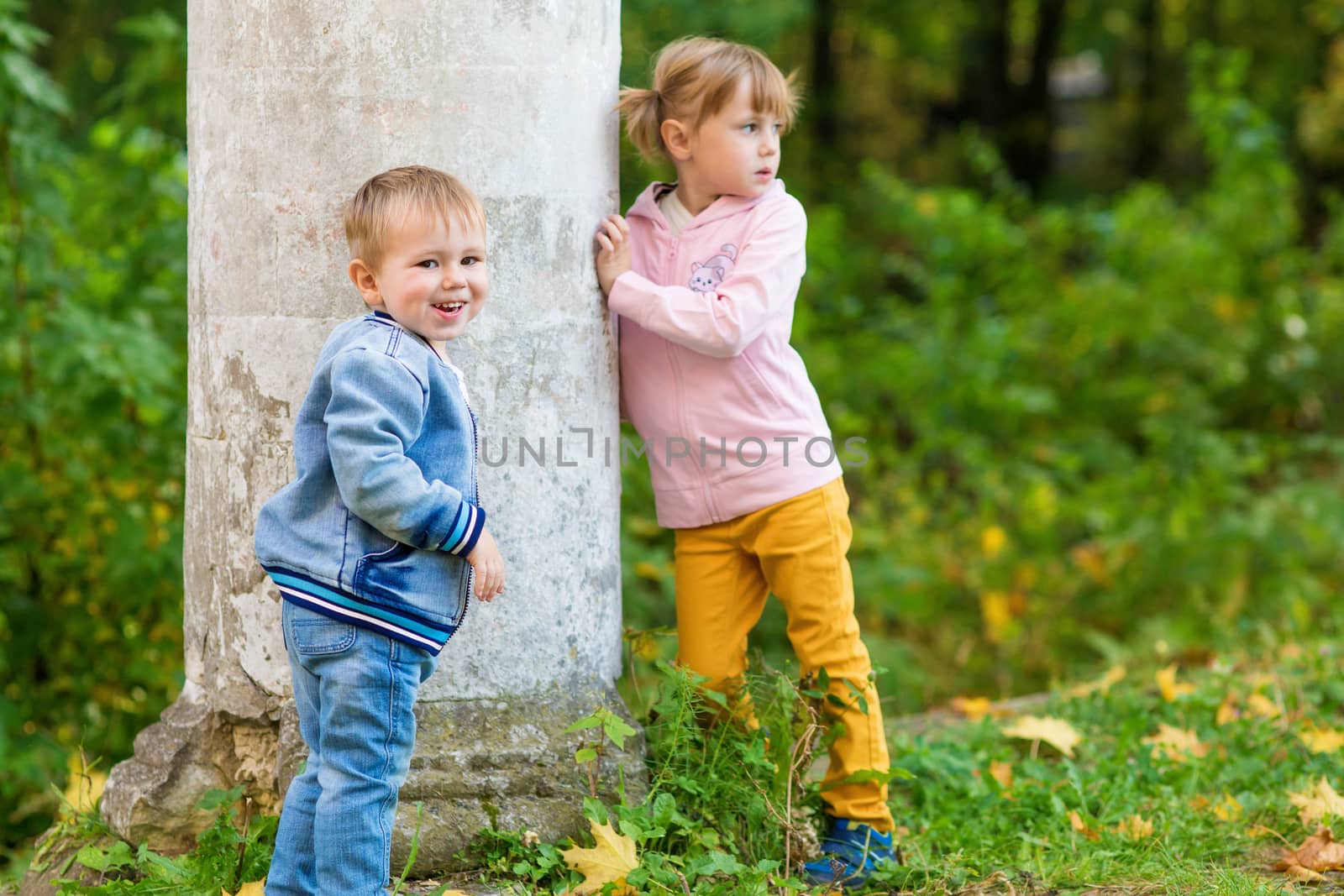 Children play near the column in the old park on an autumn walk, boy is looking at the camera smiling