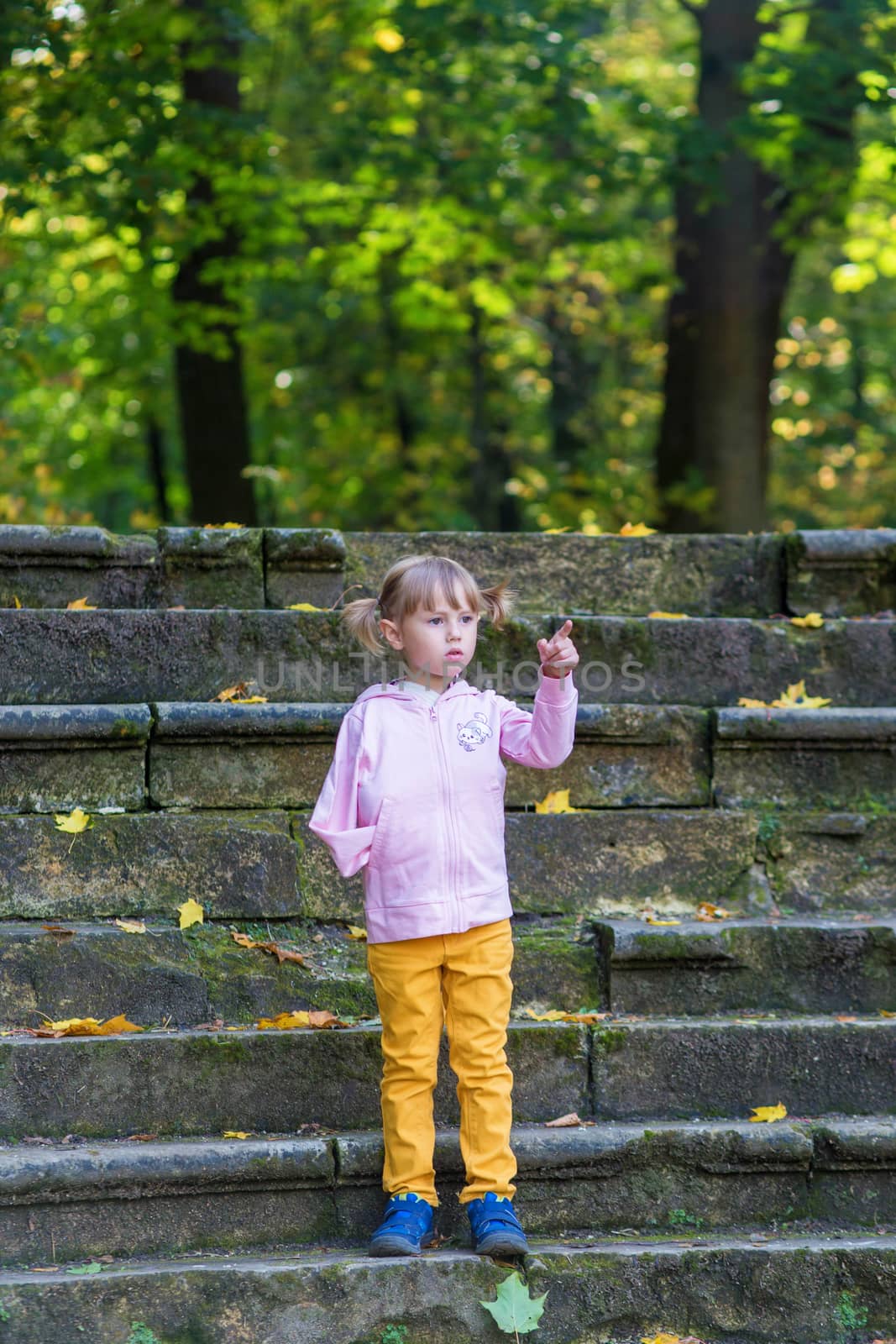 A girl with a broken arm stands on the stairs in an old park on an autumn walk
