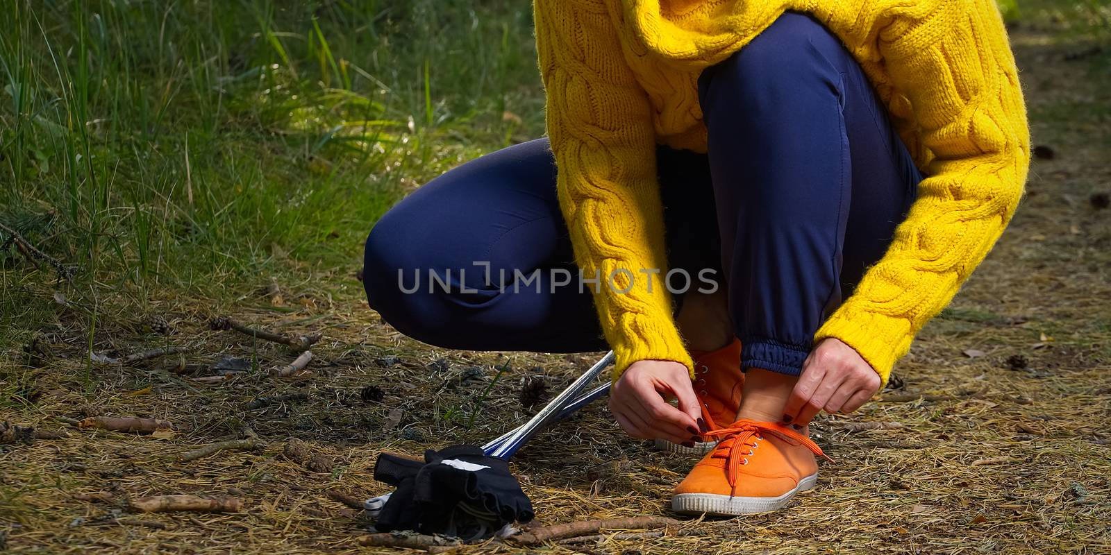 Sporty hiking woman tying shoelaces on her jogging shoes while taking a break after hiking in autumn forest. hiking concept, healthy outdoor lifestyle.