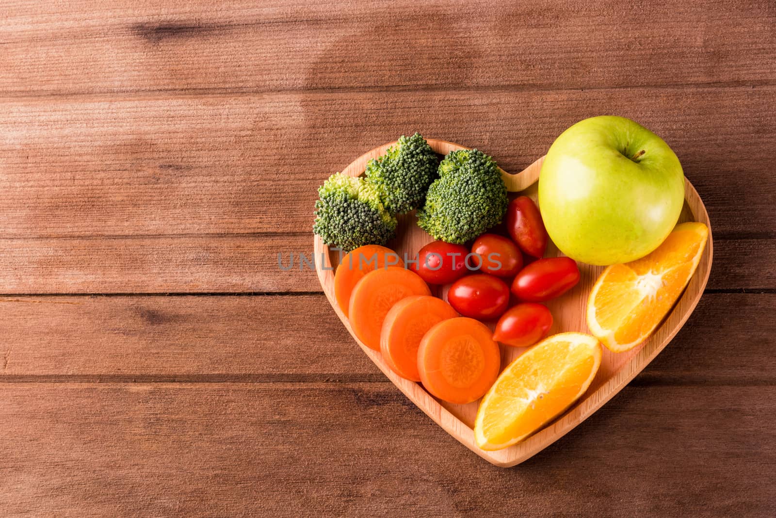 Top view of fresh organic fruits and vegetables in heart plate wood (apple, carrot, tomato, orange, broccoli) on wooden table, Healthy lifestyle diet food concept
