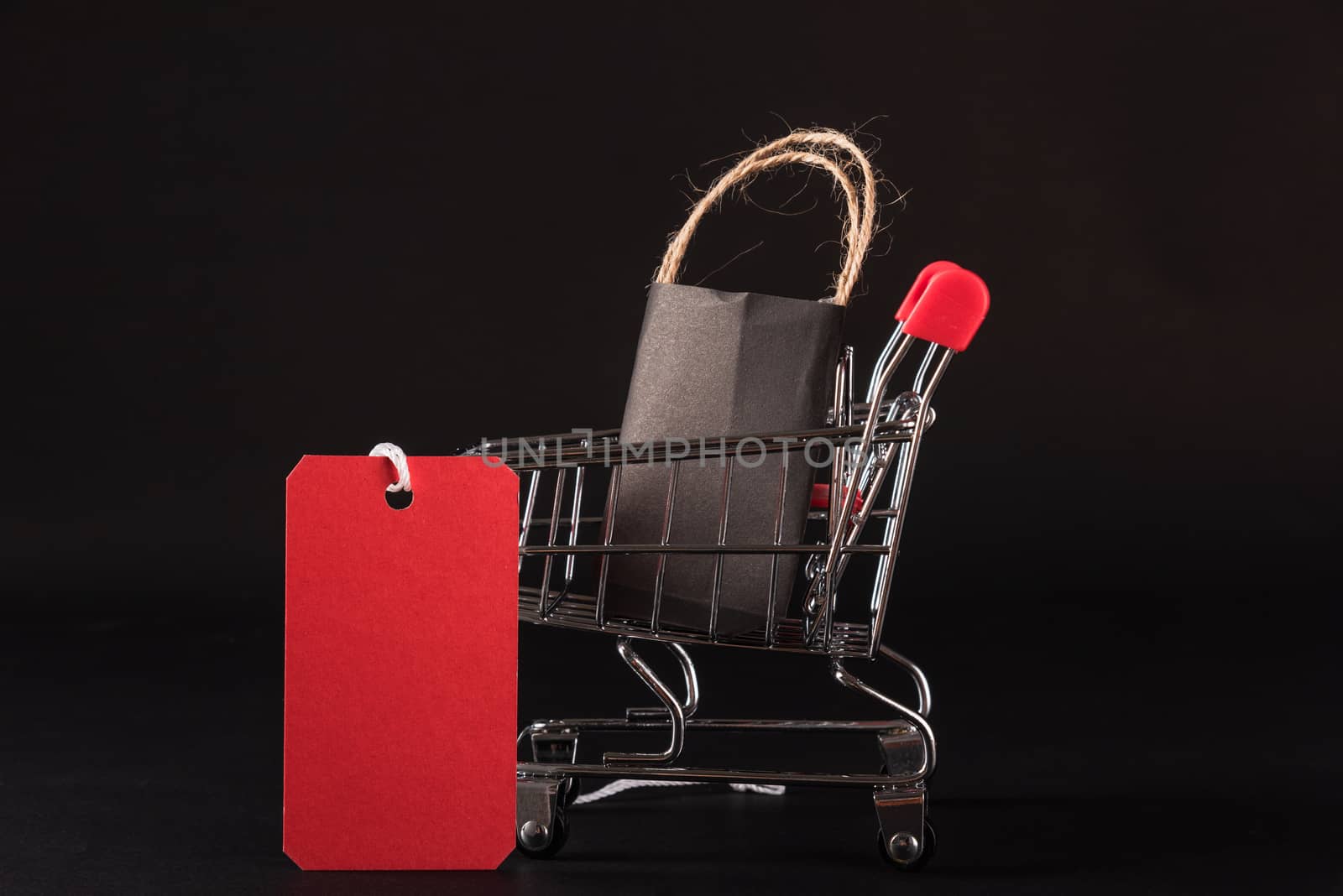 Black Friday sale shopping concept, Black shopping bags in a shopping cart and red tag, studio shot isolated on black background