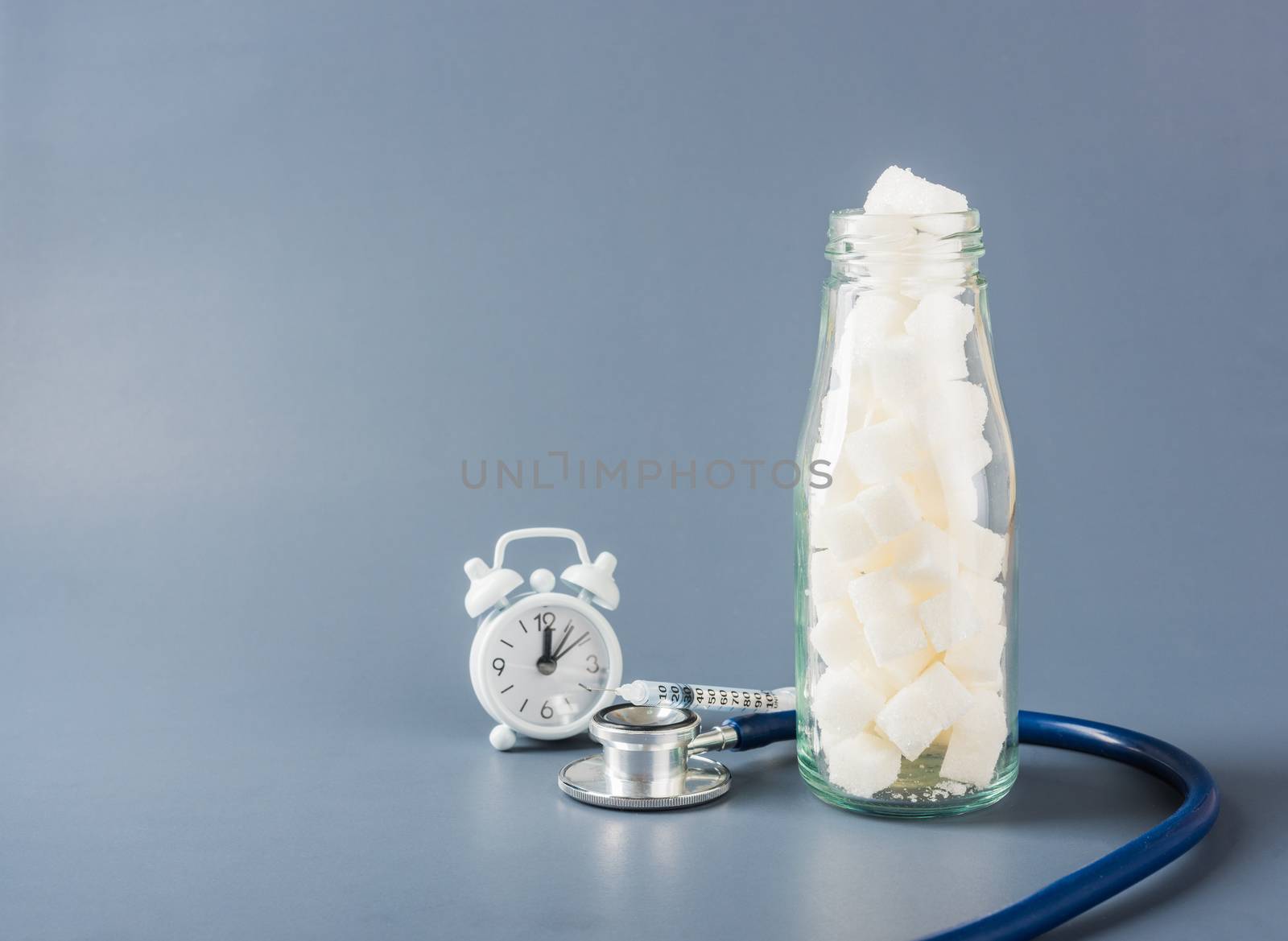 Glass bottle full of white sugar cube sweet food ingredient and doctor stethoscope isolated gray background, health high blood risk of diabetes and calorie intake concept and unhealthy drink