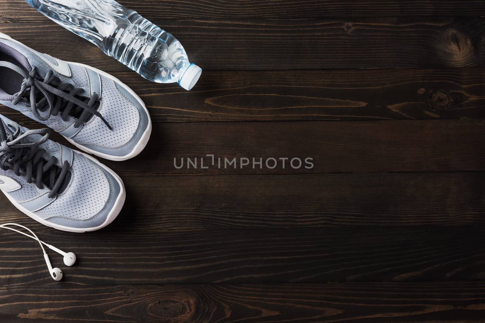 pair sports shoes, headphones and water bottle on black wood by Sorapop