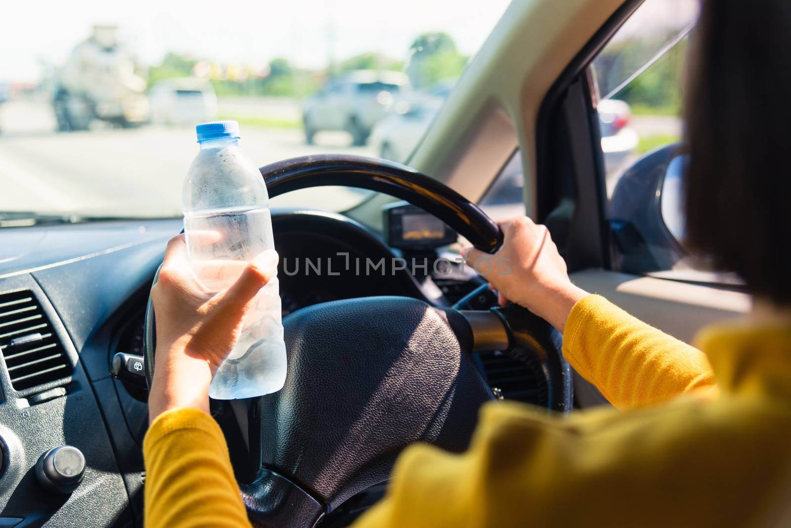 Asian woman holding a water bottle for drink while driving the car in the morning during going to work on highway road, Transportation and vehicle concept