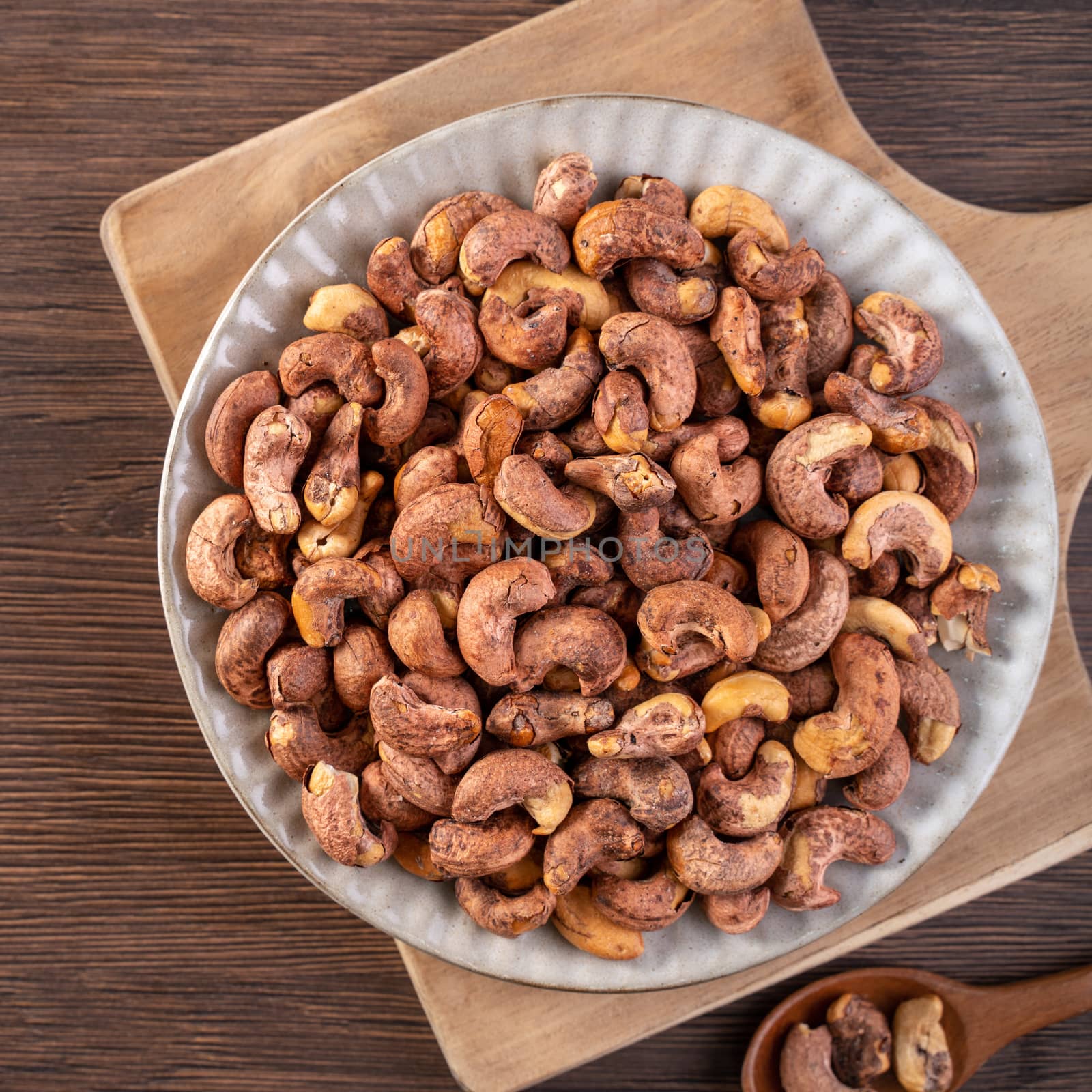 Cashew nuts with peel in a plate on wooden tray and table background, healthy raw food plate.