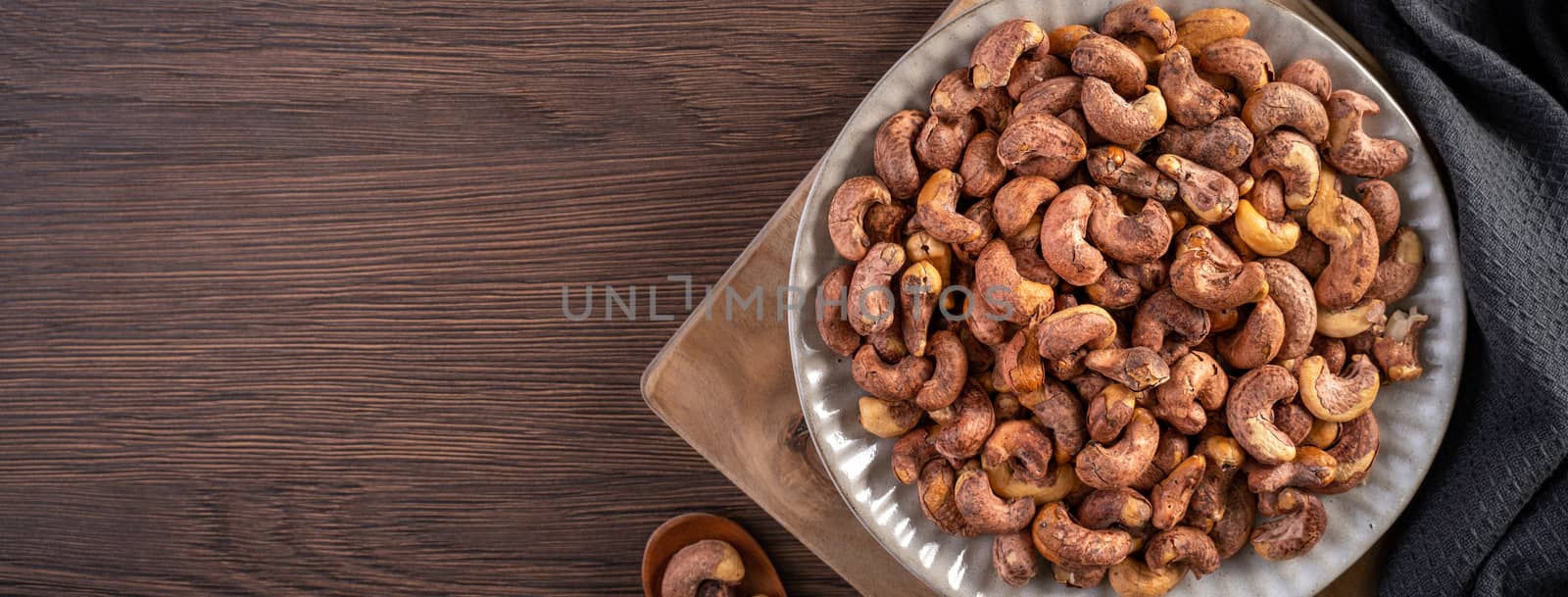 Cashew nuts with peel in a plate on wooden tray and table background, healthy raw food plate.