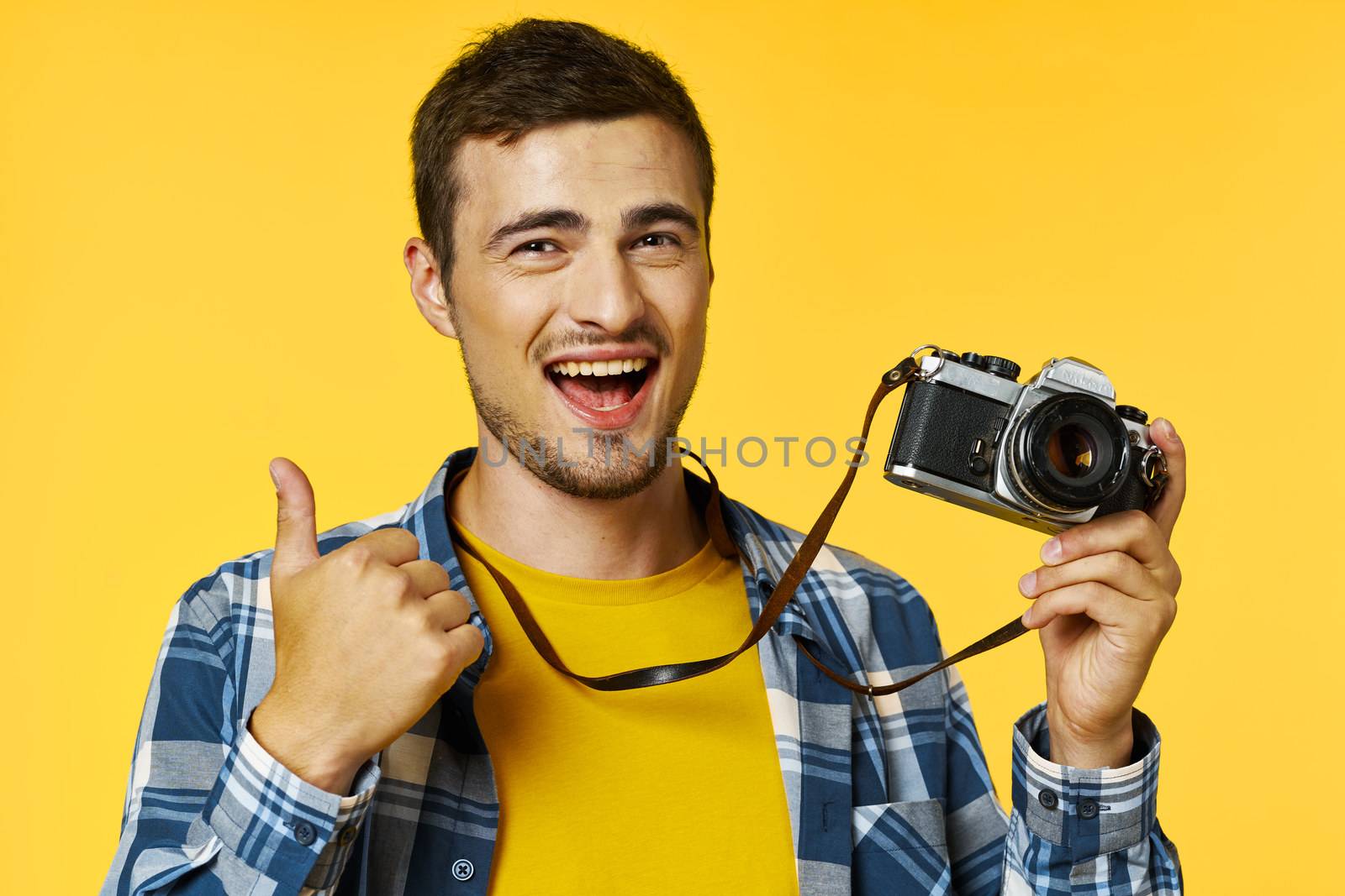A successful photographer with a camera shows a thumb and laughs at the camera