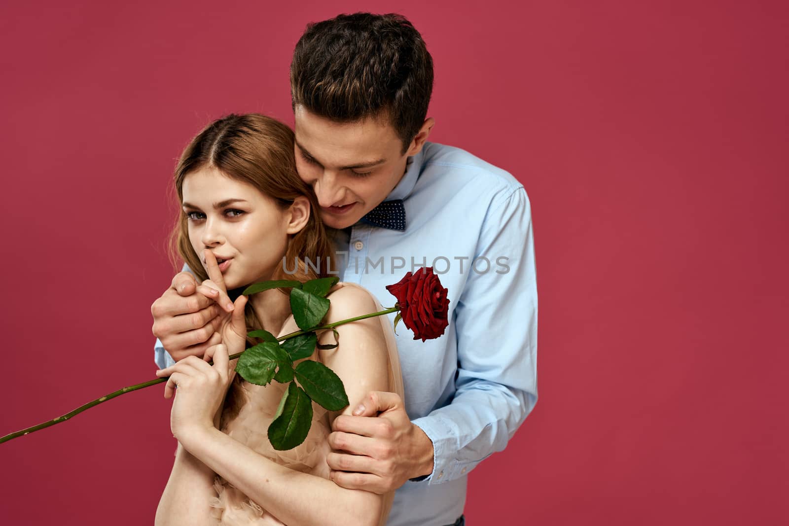 enamored man and woman with a red flower on a pink background hug each other Copy Space by SHOTPRIME