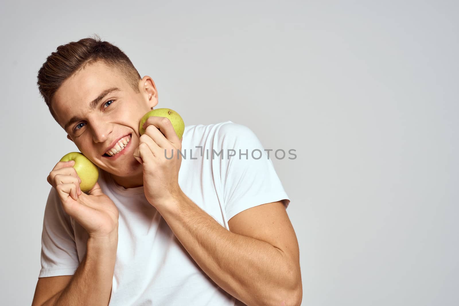 a guy with apples in his hands on a light background in a white t-shirt gesticulate with his hands smile by SHOTPRIME