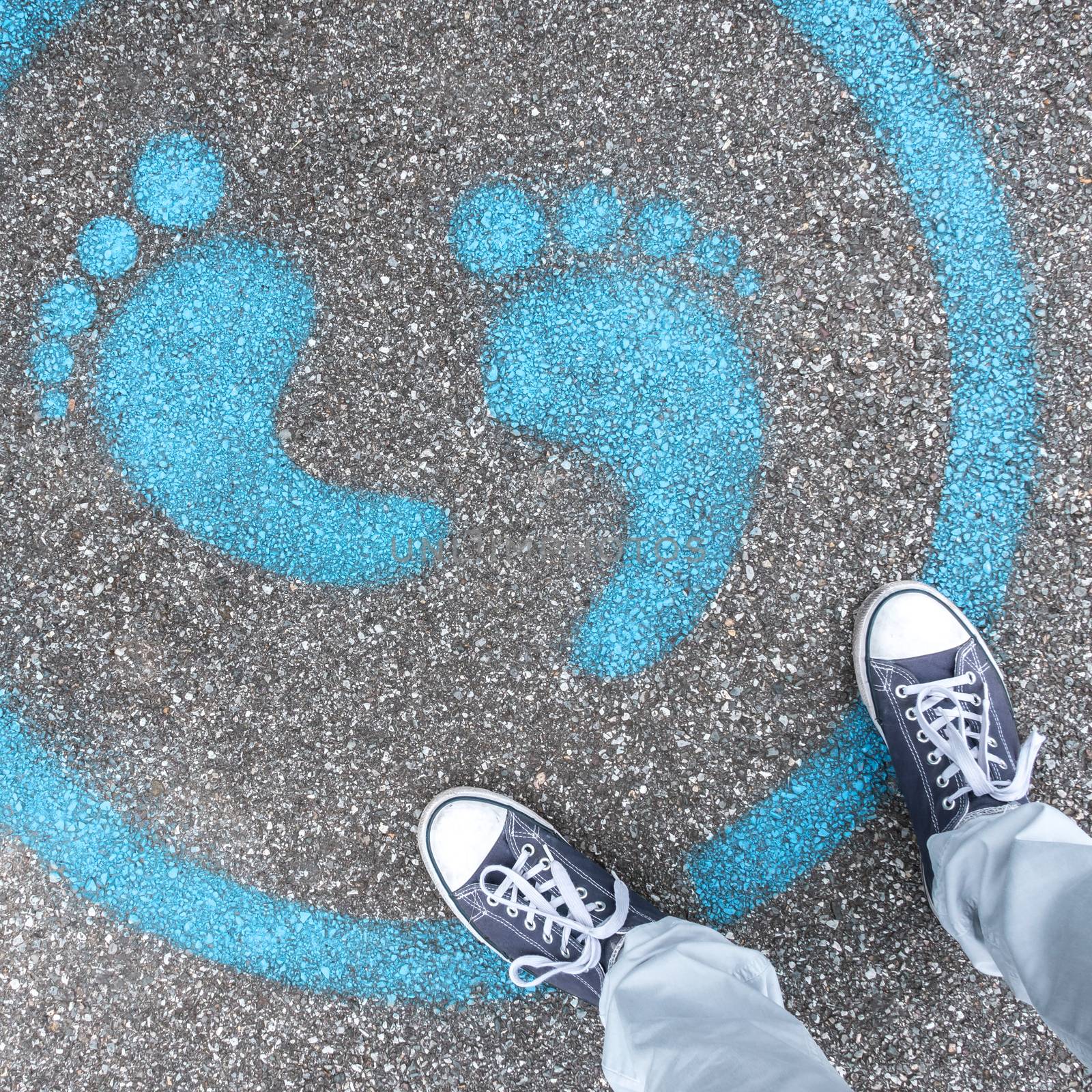 Man standing on blue dot. Sign painted on the pavement reminding users to maintain a physical distance of 3 feet / 1 meter during the COVID-19 pandemic.