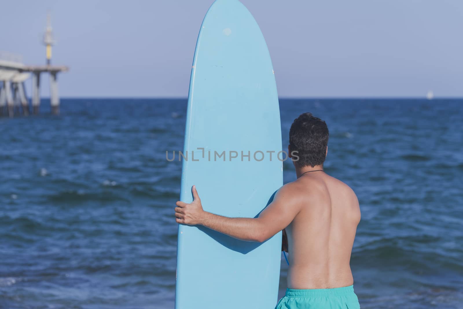 Young attractive surfer holding his surfboard at the beach
