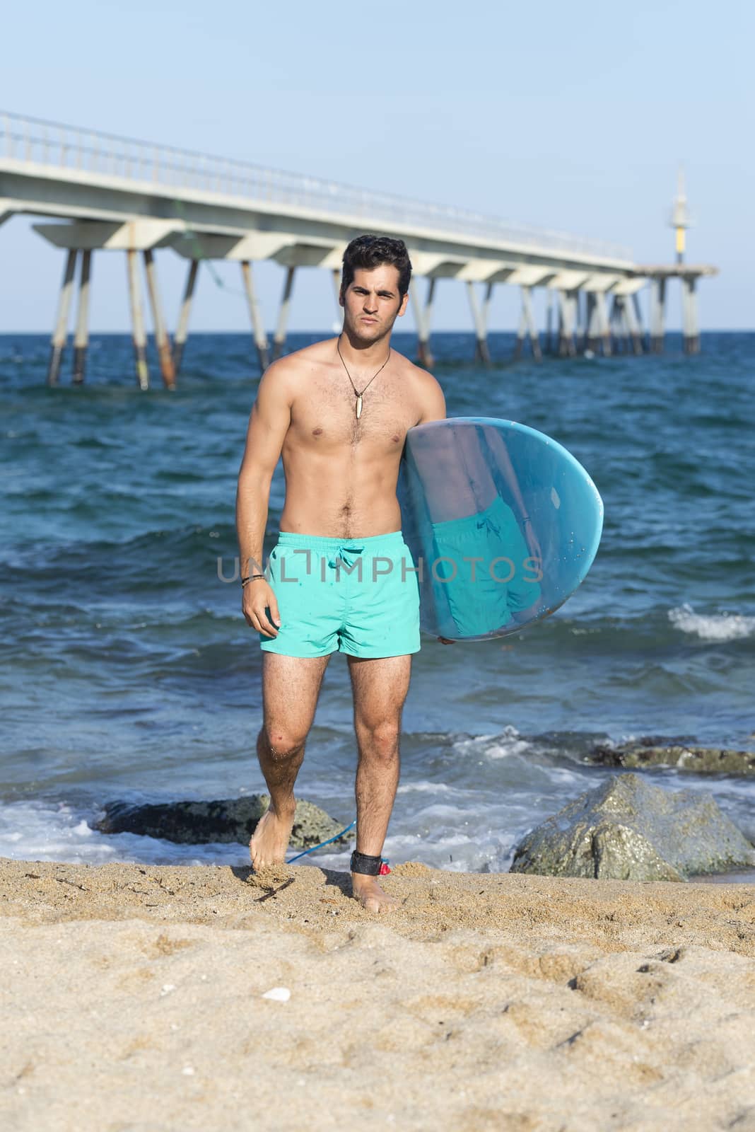 Young attractive surfer holding his surfboard at the beach