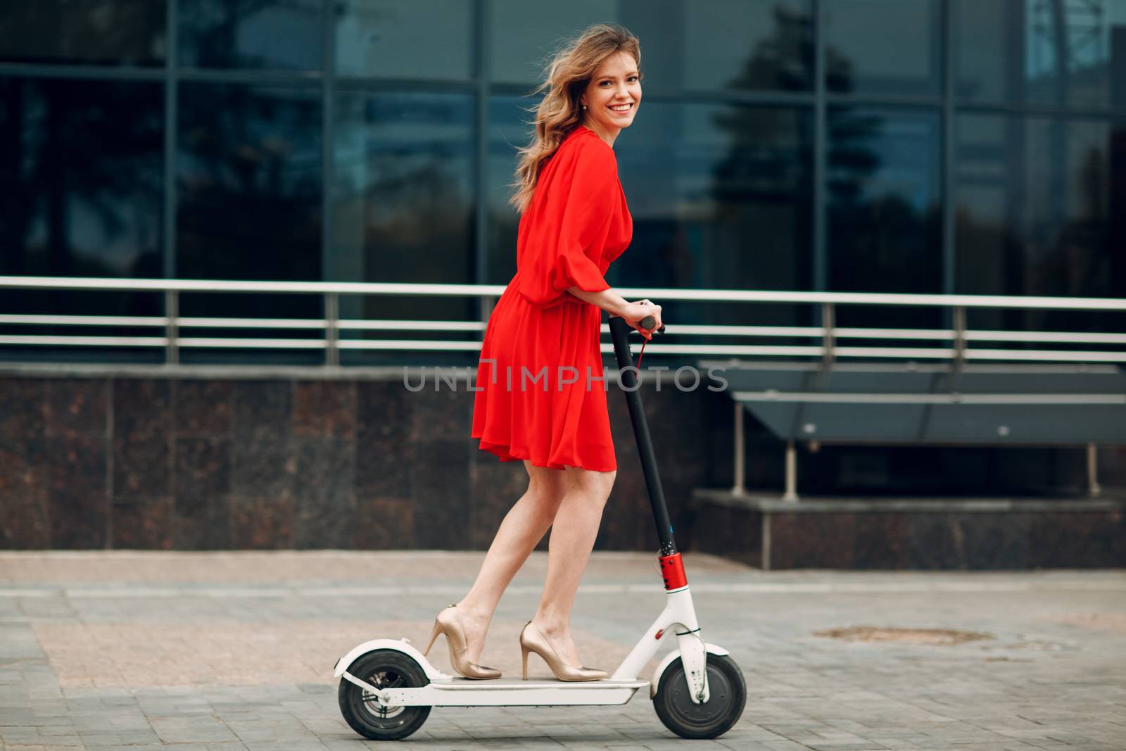 Young woman riding electric scooter in red dress at the city.