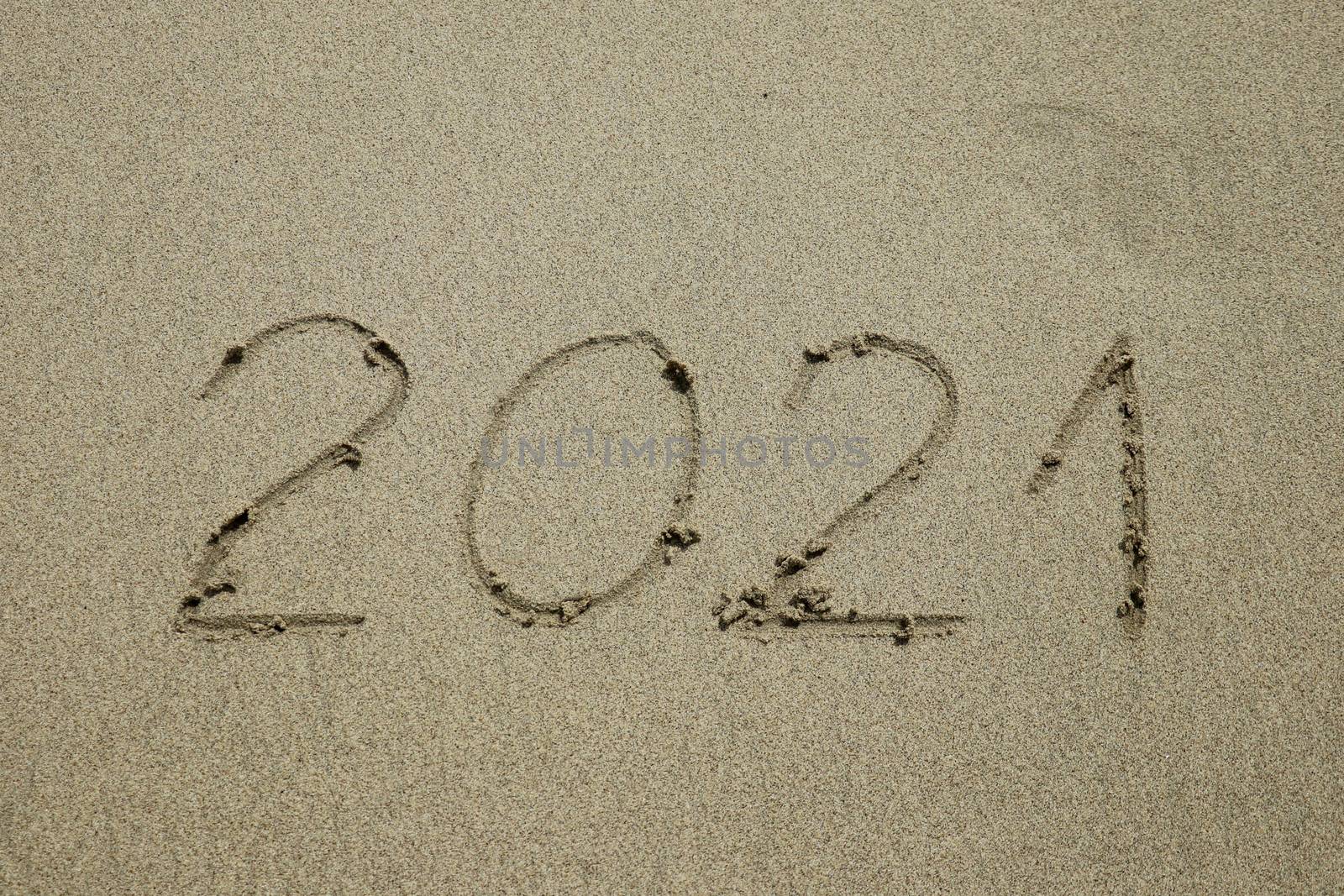 Closeup photo of 2021 numbers written on sand and footprints on sea beach. Concept of New Year, Christmas and travel on winter holidays.