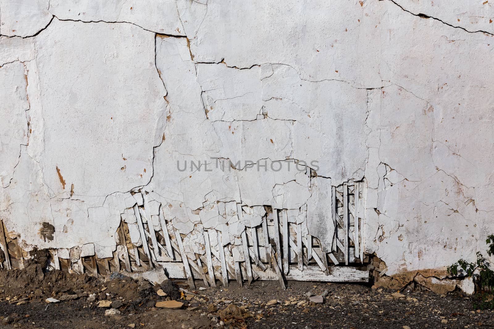 poor wattle and daub cracked stucco wall with white plaster and ground line