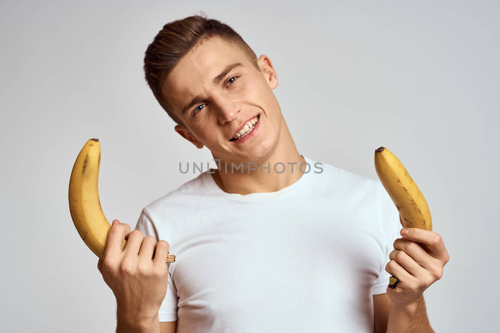 guy with a banana in his hand on a light background fun emotions light background white t-shirt model by SHOTPRIME