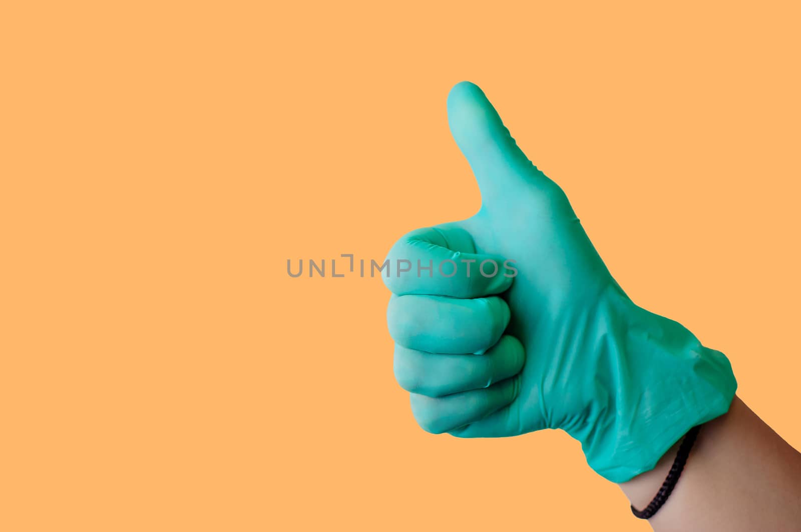 Female hand in blue latex glove makes thumbs up like gesture isolate on a light orange background. Medical health concept. Copy space