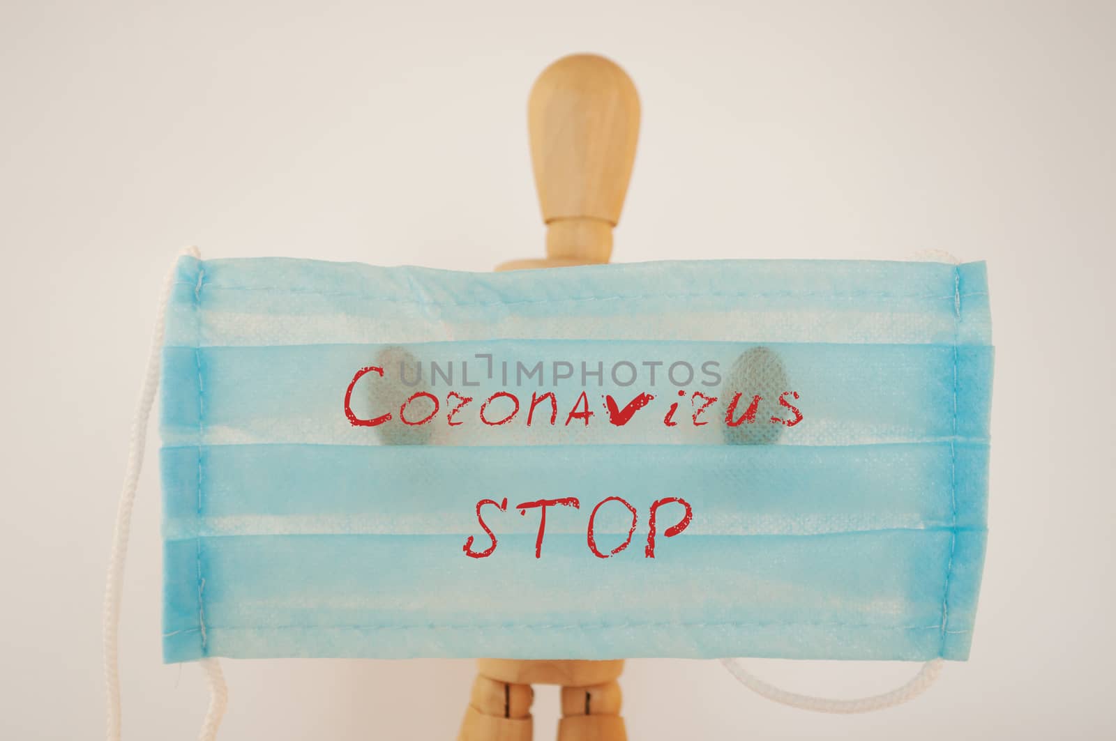 Surprised wooden man holds a blue medical protective mask with the inscription: stop, coronavirus. The concept of protection during the coronavirus pandemic. Copy space by Alla_Morozova93