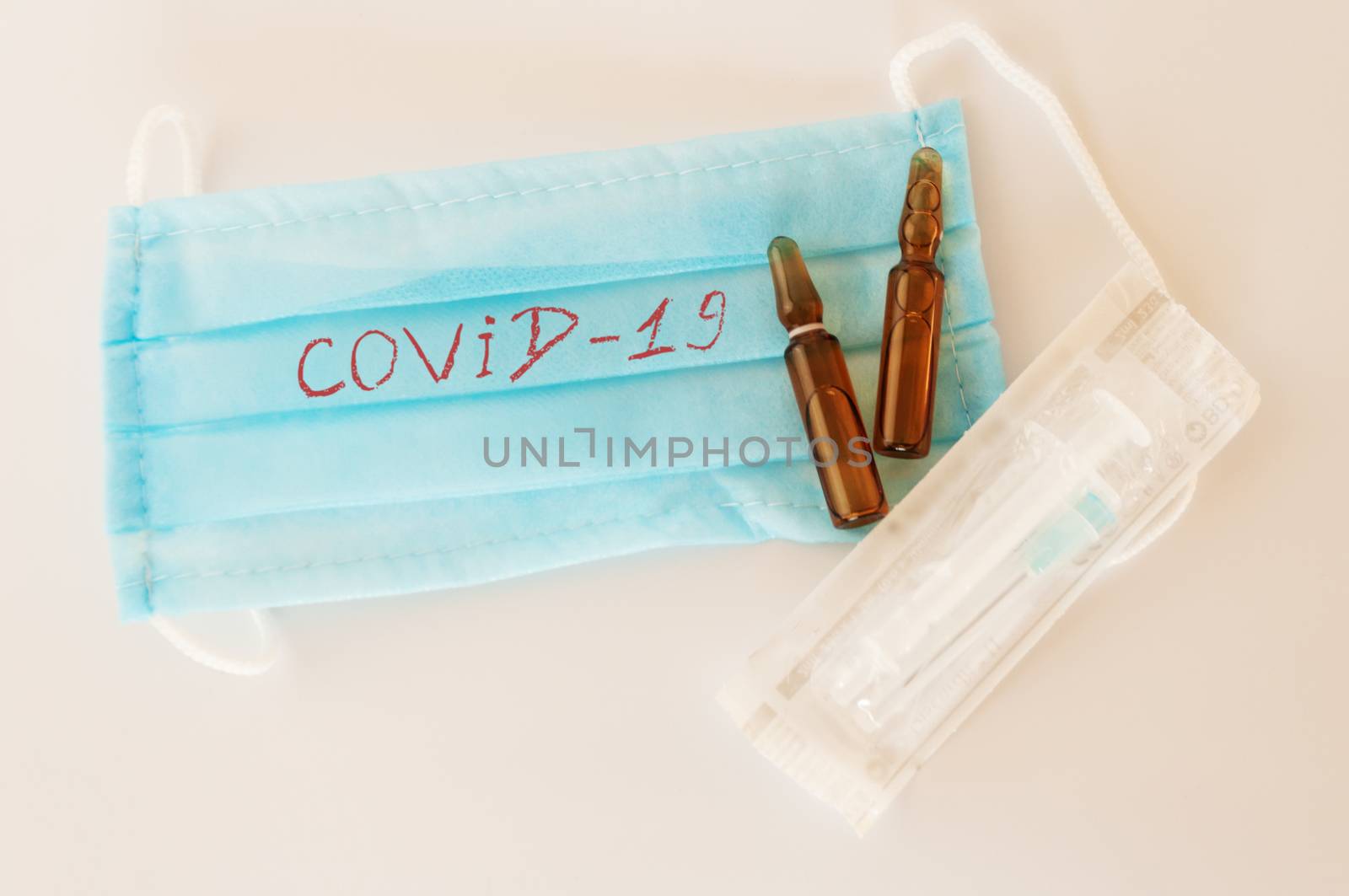 protective medical mask with the inscription covid-19, antibiotics in ampoules and a syringe. The concept of the treatment of the coronavirus pandemic. Top view. Copy space.