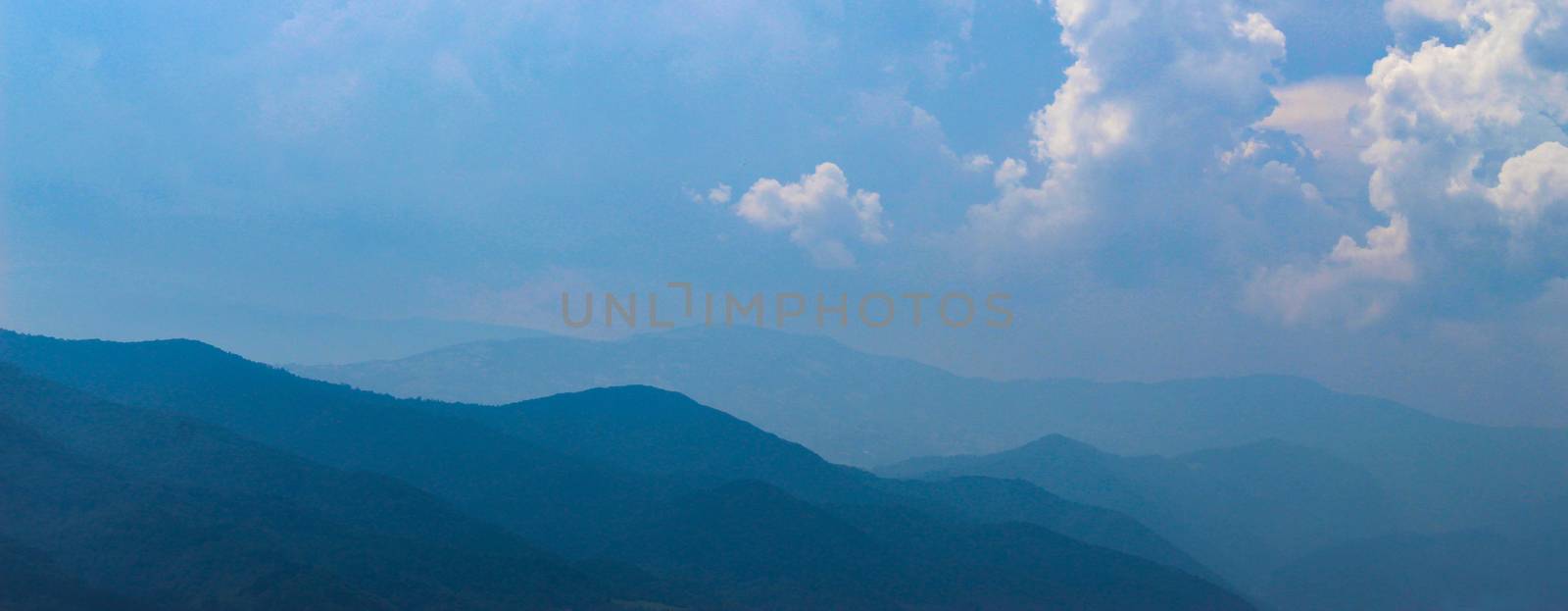 Banner of blue silhouettes of mountains in the distance, with clouds in the blue sky. Mountains and hills in the distance. by mahirrov