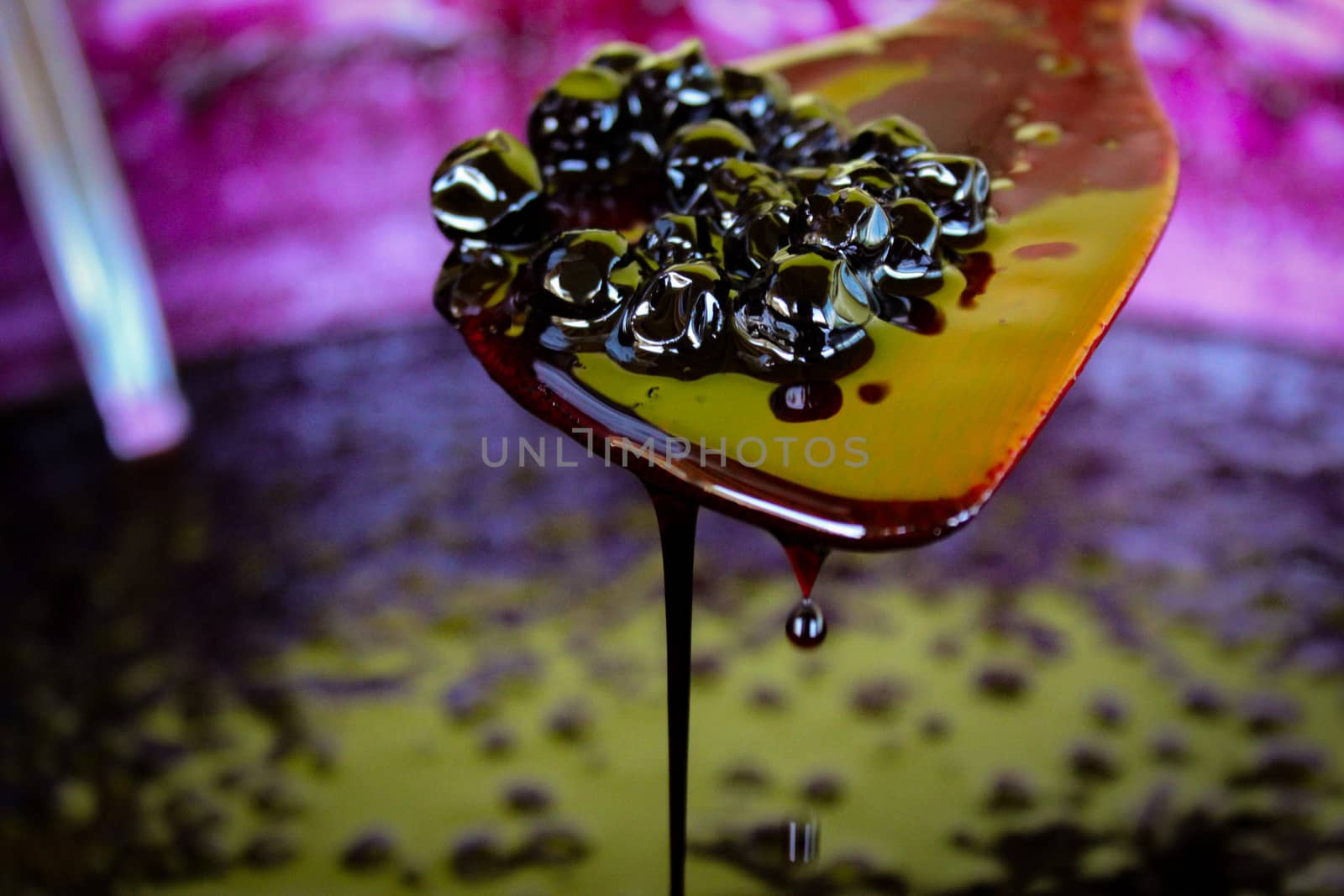 A group of chokeberry berries on a wooden cooking spoon, liquid jam leaks and drips down the spoon into a pot with chokeberry jam. by mahirrov