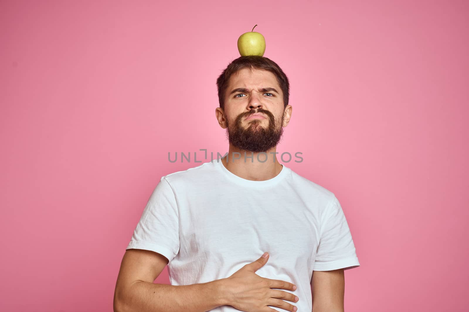 Cute man with an apple on a pink background gestures with his hands cropped white T-shirt Copy Space. High quality photo