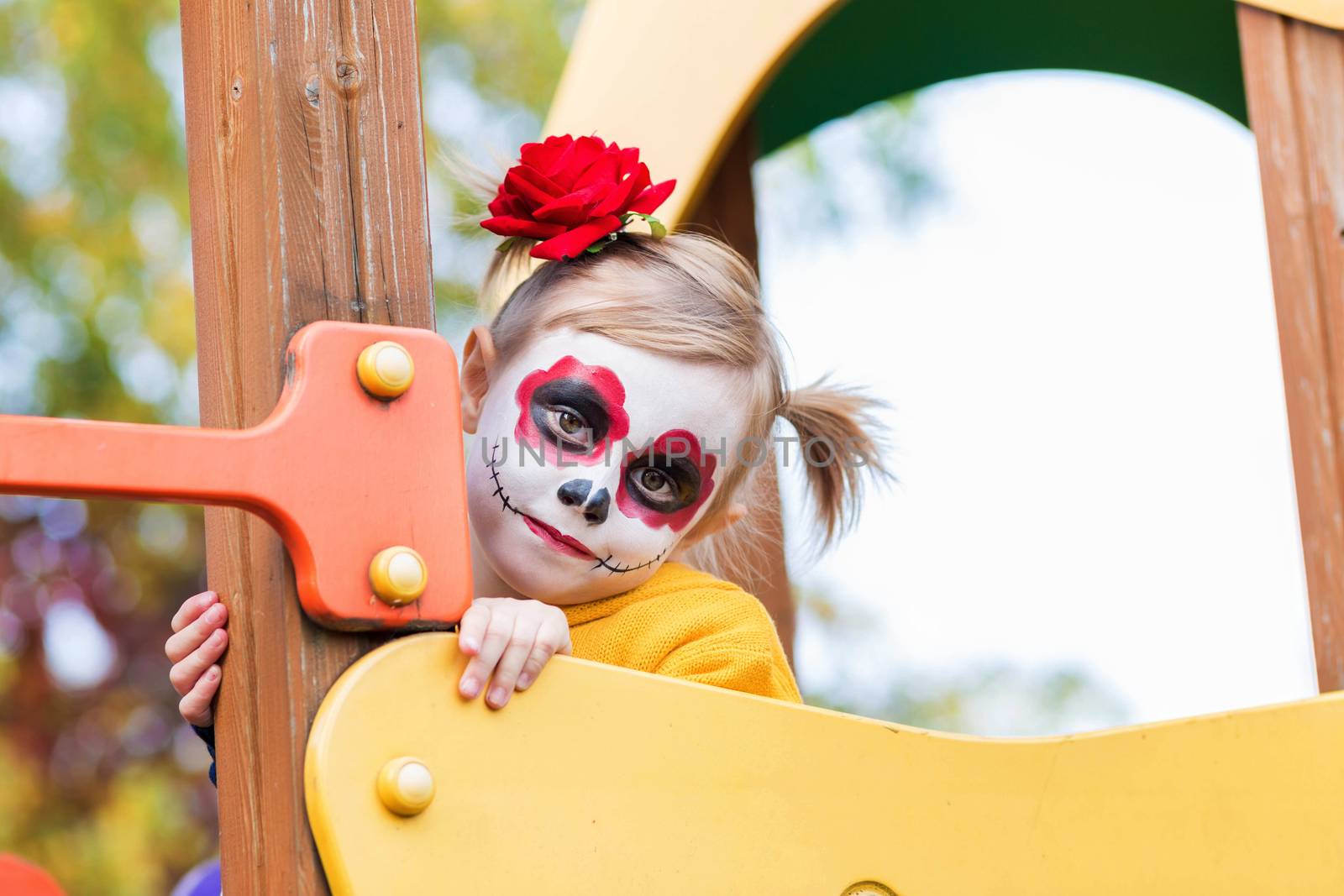 A little preschool girl with Painted Face, climbed the slide on the playground, celebrates Halloween or Mexican Day of the Dead.