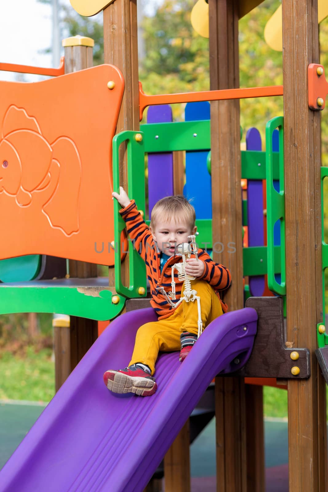 Happy Halloween. funny child with a skeleton toy in his hands and rides down a slide on the playground