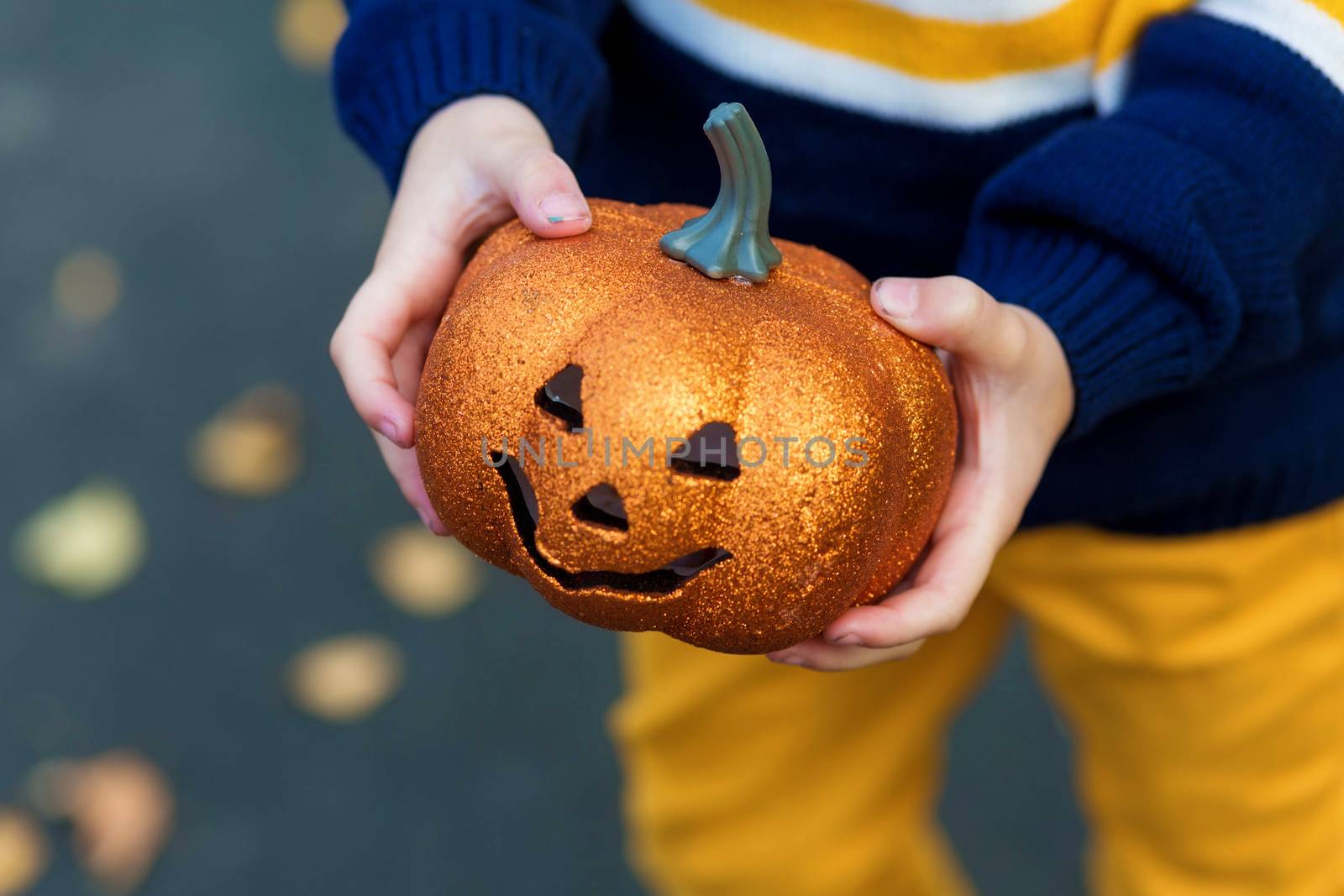 Children's hands holding a toy pumpkin lantern for the holiday halloween