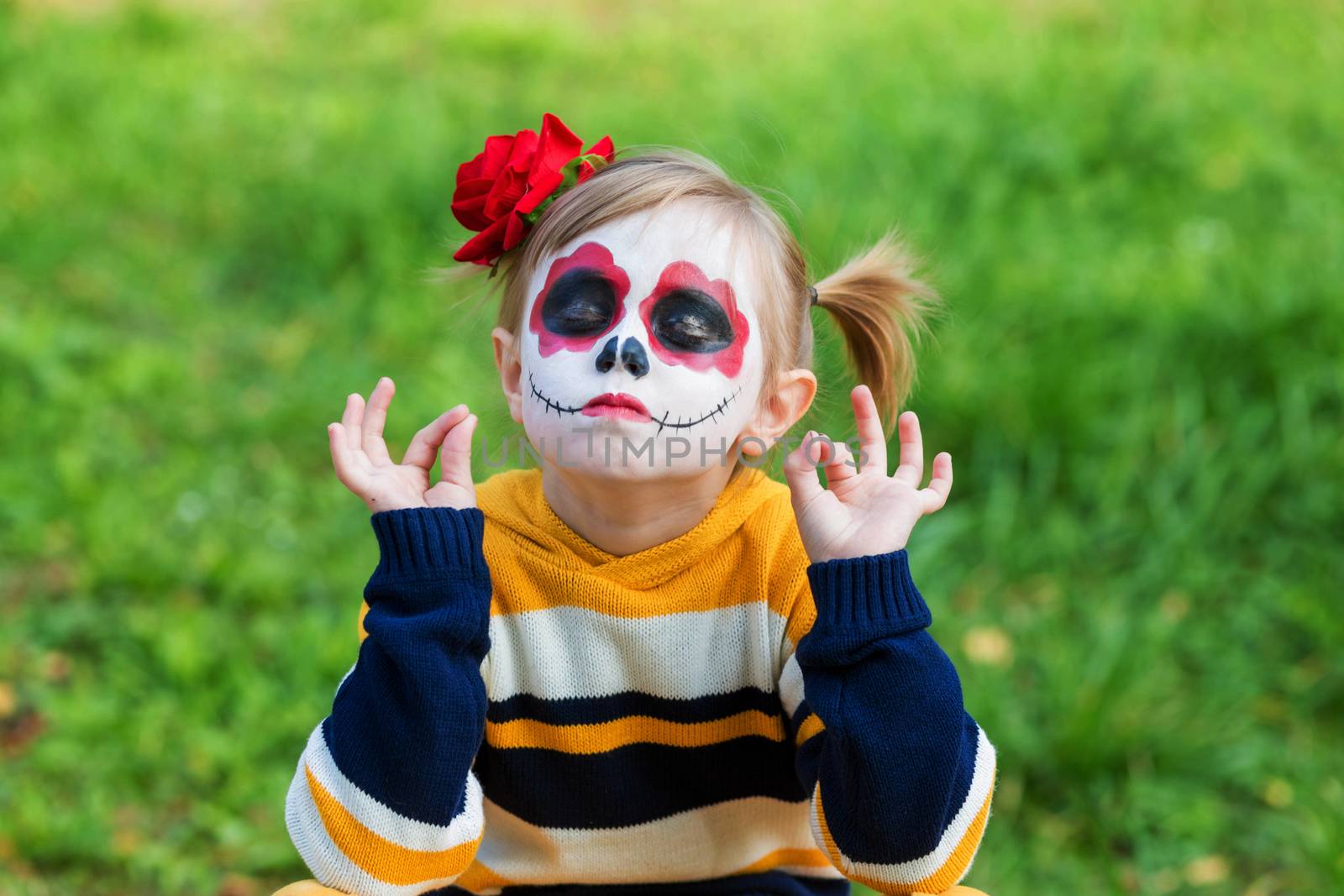 .A little preschool girl with Painted Face, smiling at the camera on the playground, celebrates Halloween or Mexican Day of the Dead.