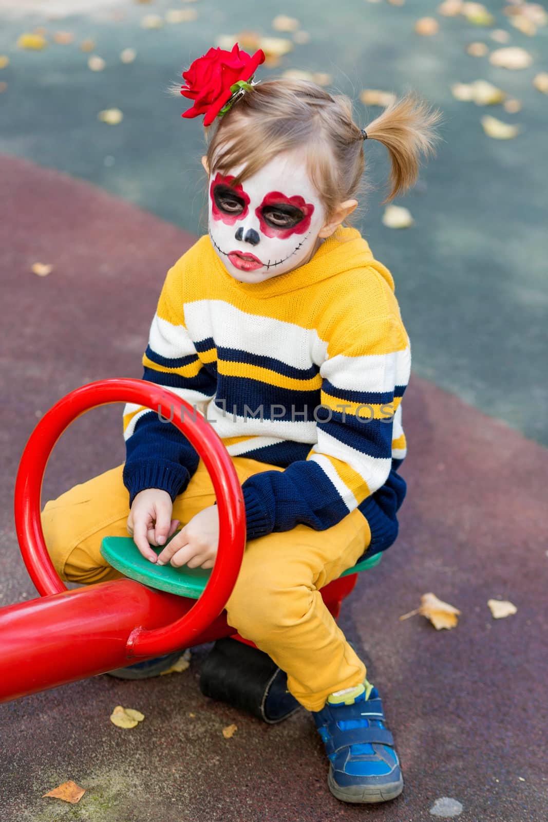 A little girl with Painted Face, rides on a swing in the playground by galinasharapova