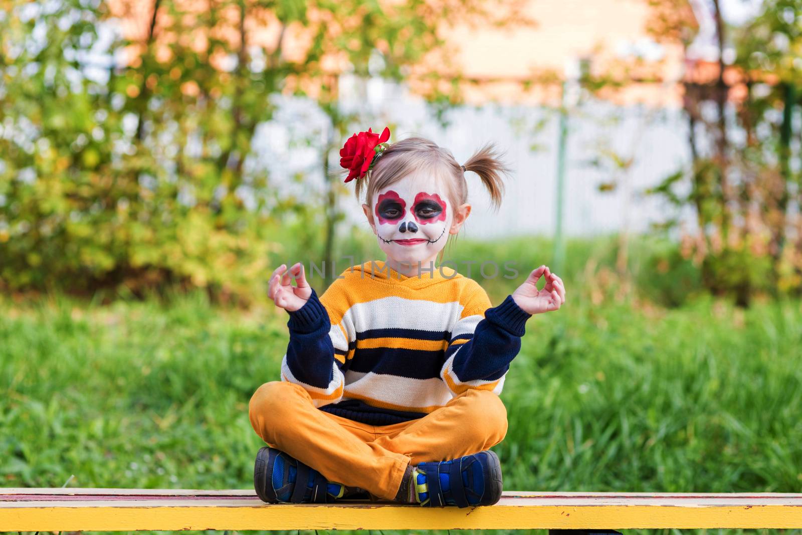 A little girl with Painted Face, sitting on a bench on Day of the Dead. by galinasharapova