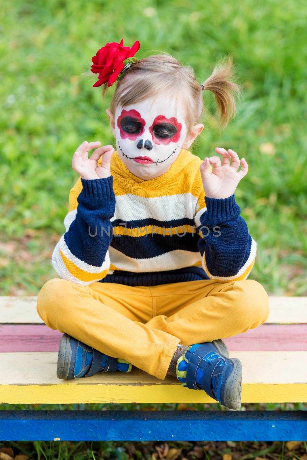 A little girl with Painted Face, sitting on a bench on Day of the Dead. by galinasharapova