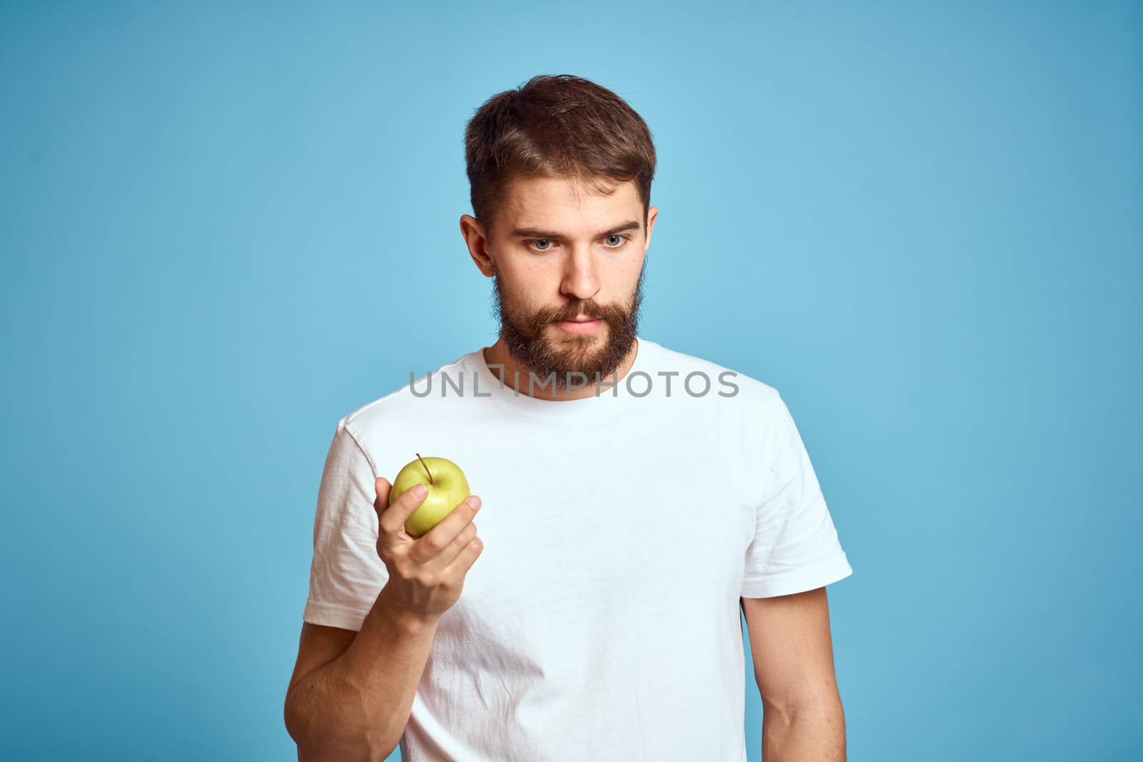 emotional Man with apple on blue background in white t-shirt cropped view. High quality photo