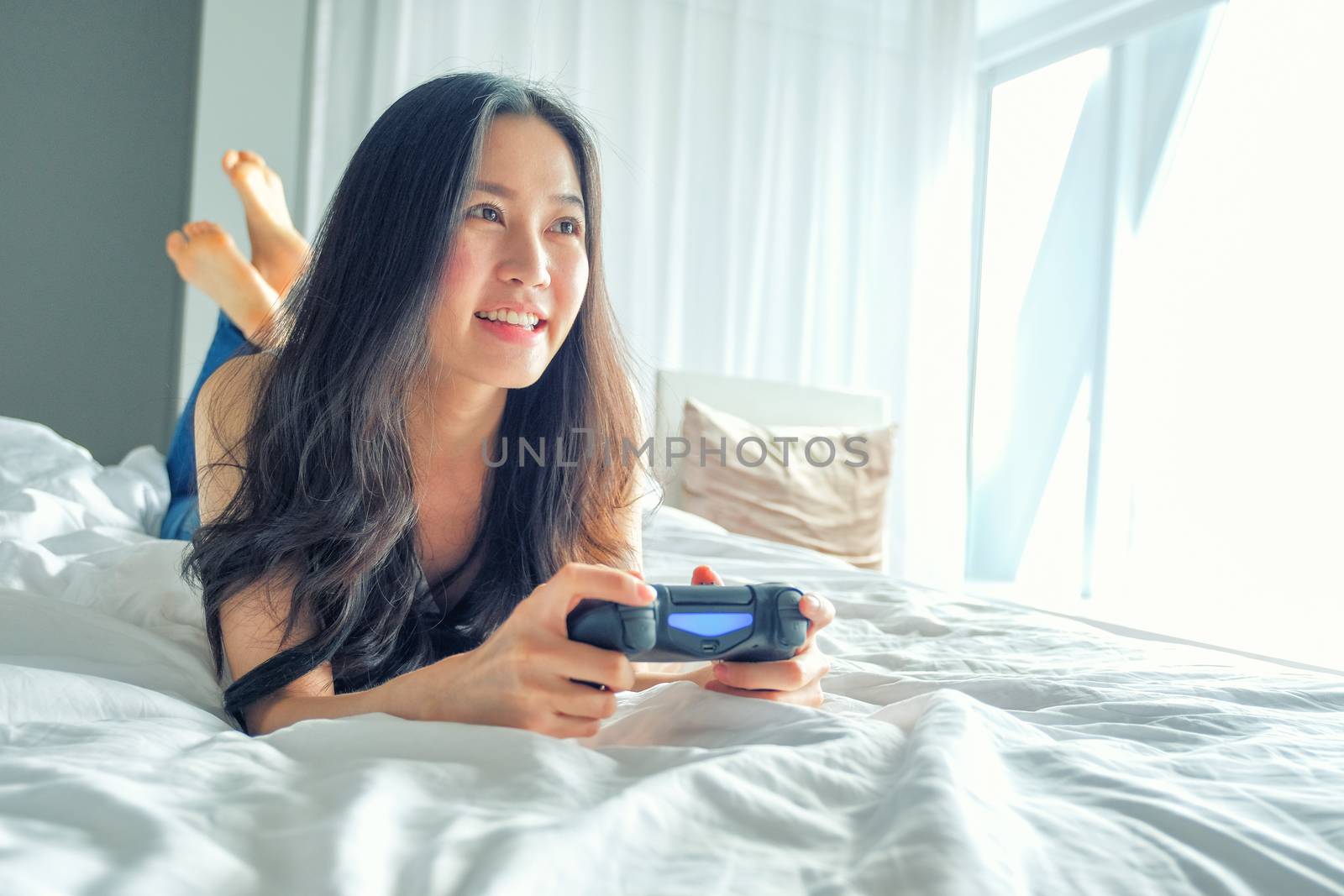 Beautiful girl playing video game on bed by Surasak