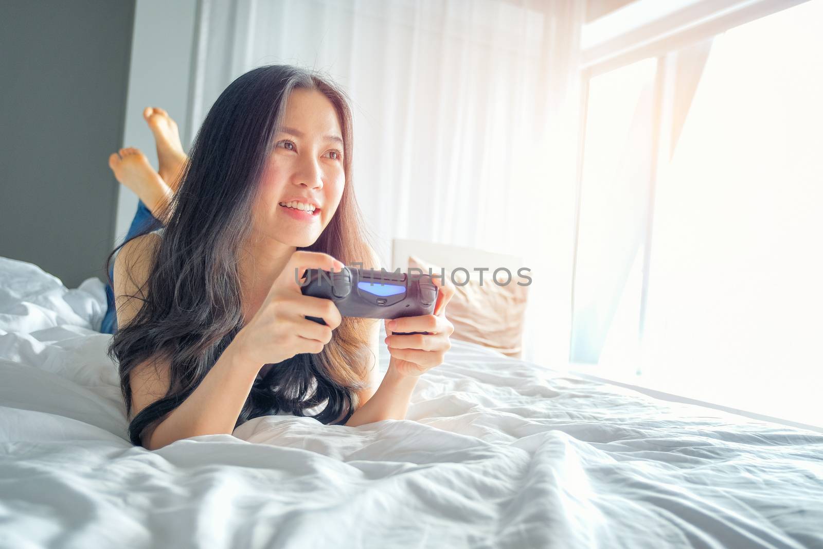 Beautiful girl playing video game on bed by Surasak