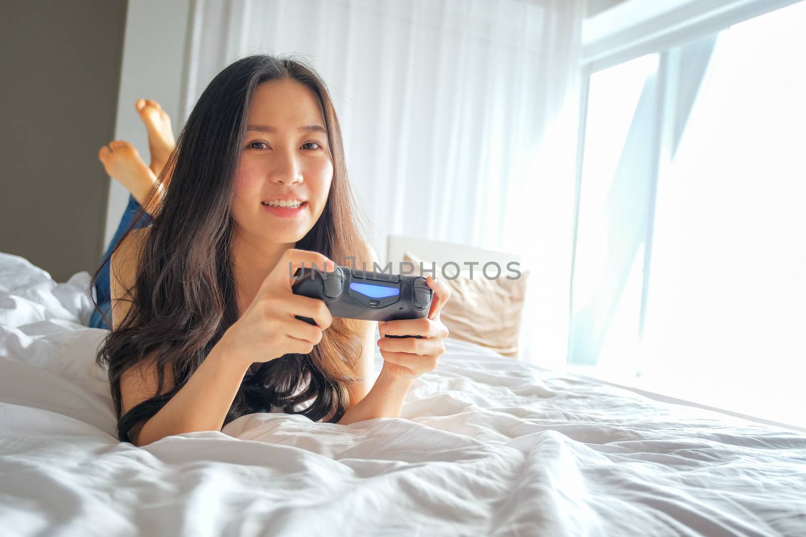 Beautiful girl playing video game on bed by Surasak