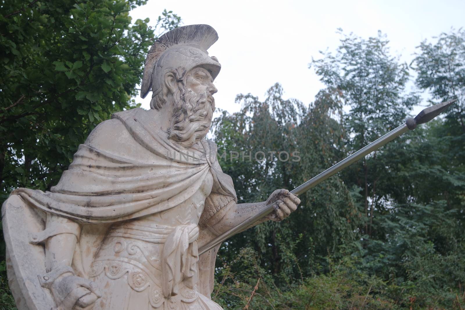 Sculpture of ancient man with harpoon in hand. Human body ancient male statue made of white marble placed in a public park