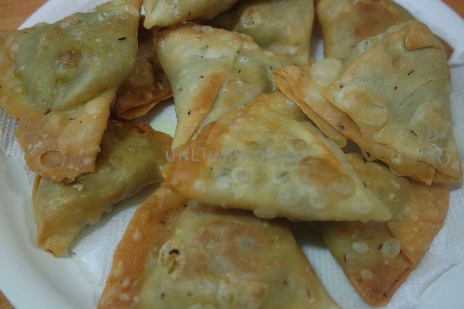 Closeup of delicious home made spicy and crunchy samosa pastries placed in a white ceramic plate on wooden floor