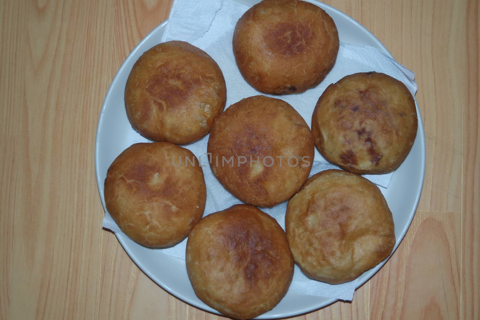 Closeup view of homemade tasty potato bread rolls bun placed in a white plate over a wooden floor.
